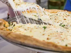 Hvid pizza uden tomat med smeltet ost og hakkede krydderurter; et stykke løftes op, så osten trækker i tråde
