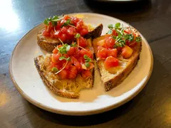 Tre skiver ristet brød med hakket tomat og friske grønne spirer på en lys tallerken