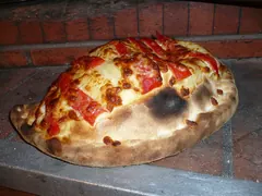 Foldet calzone med gyldenbrun bund, ost og røde peberstrimler ovenpå, på en stenhylde foran en murstensvæg