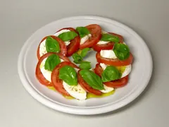 Skiver af tomat og mozzarella lagt i en ring med basilikumblade og olivenolie på en hvid tallerken