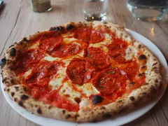 Pizza med tomatsauce, mozzarella og skiver af salami, bagt med mørke bobler i kanten