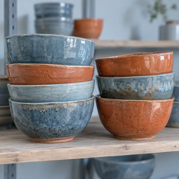 En stabel glaserede skåle i blågrå og terracotta nuancer på en træhylde